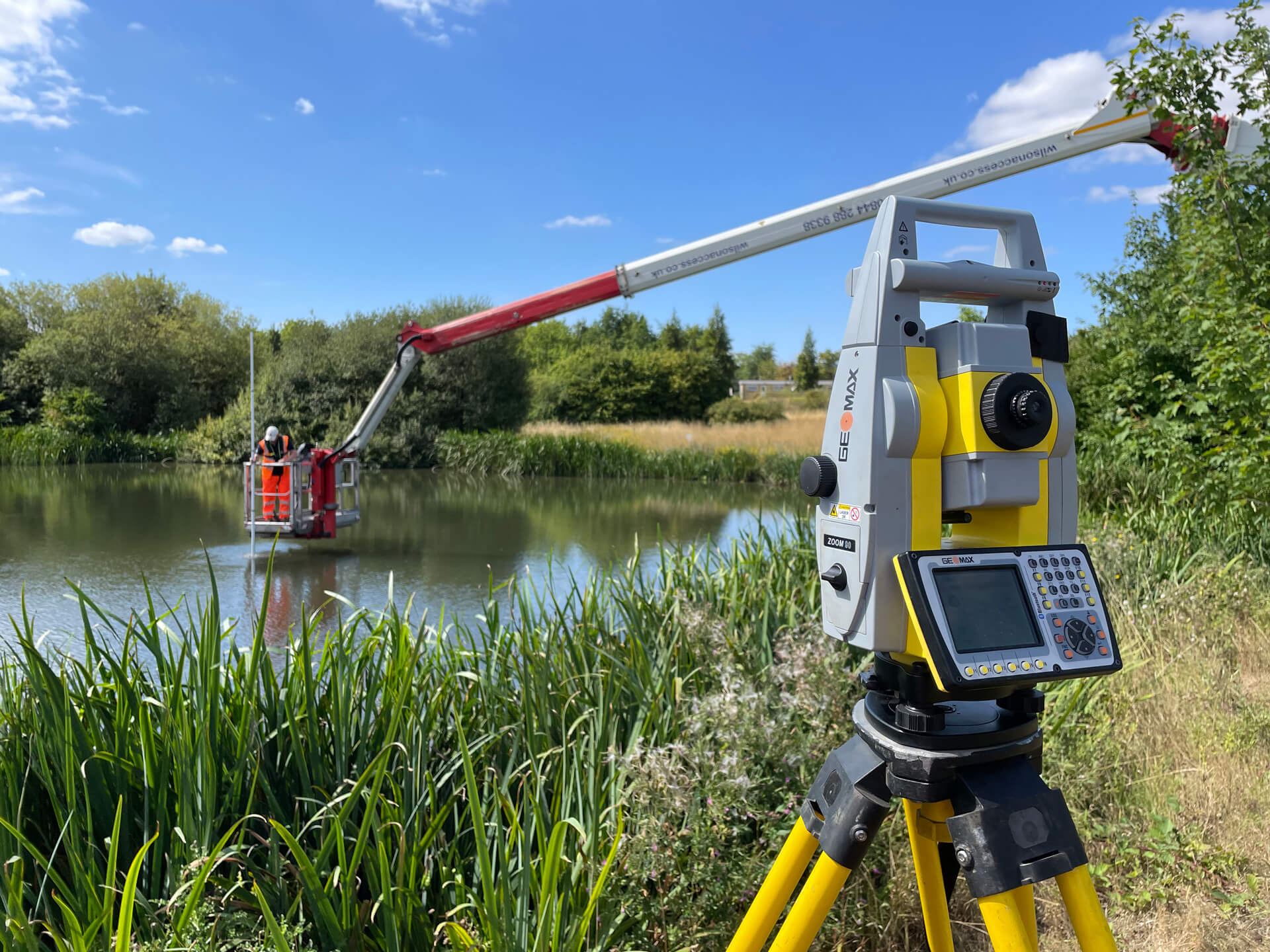 Geomax station in front of a large pond with cherry picker standing over it in the background